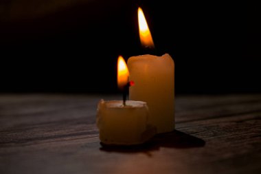 Üçgen şeklinde dizilmiş yanan mumların yakın çekimi. Koyu bir zemin, yumuşak bir alan derinliği ve şeffaf bir balmumu ile parlak alevler kontrastı samimi, atmosferik bir sahne yaratıyor..