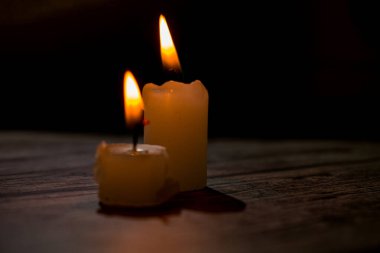 Üçgen şeklinde dizilmiş yanan mumların yakın çekimi. Koyu bir zemin, yumuşak bir alan derinliği ve şeffaf bir balmumu ile parlak alevler kontrastı samimi, atmosferik bir sahne yaratıyor..