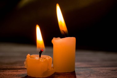 Üçgen şeklinde dizilmiş yanan mumların yakın çekimi. Koyu bir zemin, yumuşak bir alan derinliği ve şeffaf bir balmumu ile parlak alevler kontrastı samimi, atmosferik bir sahne yaratıyor..