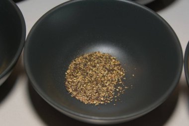 Yakın çekim, koyu gri bir seramik kasenin dibindeki siyah biberi beyaz bir tezgahta gösteriyor..