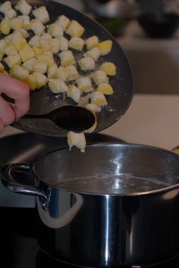 Siyah kaşıkla siyah bir kaşık kullanarak siyah bir tabaktan kayan patatesli gnocchi ile paslanmaz çelik bir su kabına konan bir fotoğraf..
