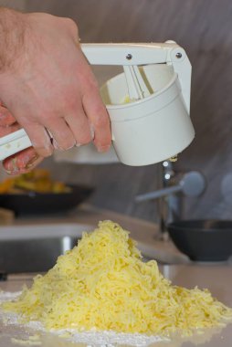 Bir insanın elleri, mutfak tezgahındaki beyaz un yığınına pişmiş sarı patatesleri bastırmak için beyaz plastik bir elle patates ezici kullanır..