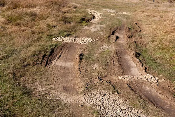 Kırsal yolda araba izleri ve çakıllar görülebilir..