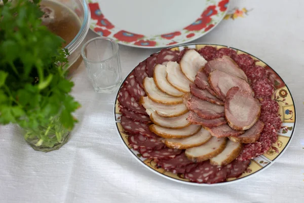 Et, tabakta dilimlenmiş sosis. Masadalar. Beyaz bir masa örtüsüne karşı.