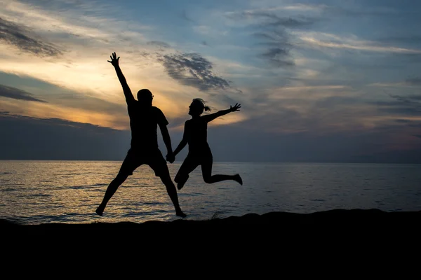 Pareja silueta saltando en la playa — Foto de Stock