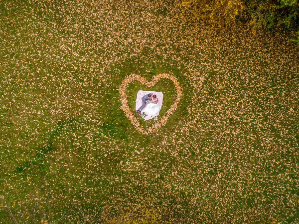 Vista aérea de matrimonio pareja acostado en una forma de corazón de otoño hojas bosque dron foto amor romántico — Foto de Stock