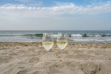 Korsika, Fransa 'da romantik bir ortamda iki kadeh şarap mavi bulutlu gökyüzünün önündeki okyanus dalgalarını seyrediyor.