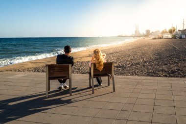 Banklarda oturan çift, İspanya 'nın Badalona şehrinde gün batımını seyrediyor.