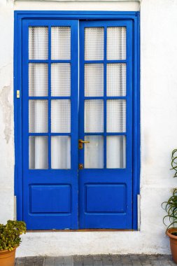 Çiçek saksıları olan beyaz bir duvarda antik mavi ahşap bir kapı. Akdeniz köyü, sakin ve sakin..