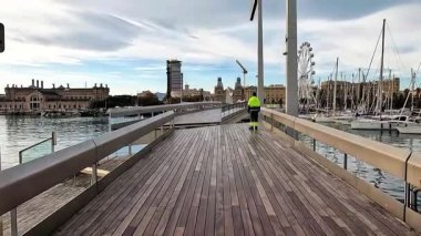 Barcelona, İspanya-24 Kasım 2025. İspanya, Barcelona 'da Rambla de Mar' ın yüzen tahta köprüsünün ikonik çekimi. Bir işçi ya da güvenlik görevlisi kaldırımda duruyor..