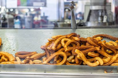 Bir sokak yemekhanesinde cam bir vitrinin arkasında churros veya porra olarak bilinen lezzetli, altın sarısı hamur tatlısı yığını..