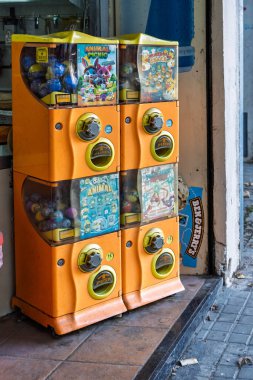 Barselona, İspanya-22 Kasım 2025. Şehir kaldırımındaki bir dükkanın önünde renkli çıkartmalı dört adet turuncu plastik kapsül oyuncak otomatı..