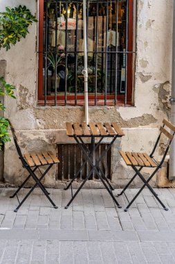 Küçük katlanır ahşap masa ve iki sandalye şehrin kaldırımında dokulu bir duvara karşı dizilmiş.