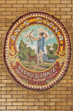 Duvarda renkli dairesel bir mozaik. Tanrıça Diana 'yı İspanyol anason imalathanesinin reklamı olarak tasvir ediyor..