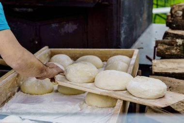 Yuvarlak hamur toplarıyla dolu ahşap bir kutu, una bulanmış, pişirmeye hazır, arka planda kütükler var.