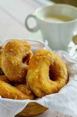 Arka planda bulanık bir bardak süt ve şekerli çöreklerden oluşan dikey bir kompozisyon..