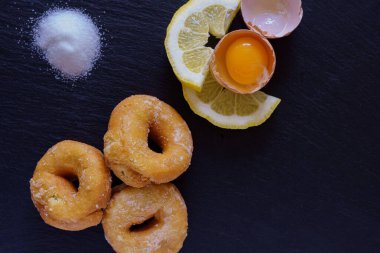 Taze pişmiş çörekler çiğ yumurta sarısı, limon dilimleri ve siyah bir levha yüzeyinde şeker ile birlikte sunulur..