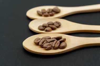 Siyah arka planda kavrulmuş kahve çekirdekli üç tahta kaşık, yakın plan, sığ alan derinliği
