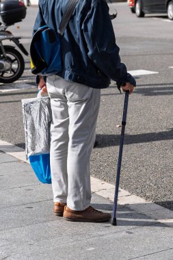 Barselona, İspanya - 14 Şubat 2026: Yürüyen bir baston ve alışveriş çantası tutan yaşlı bir vatandaşın cesedi, bir kavşakta bekliyor.