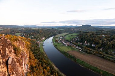 Gün batımında Sakson İsviçre manzarası. Sonbahar mevsiminde Doğu Almanya 'nın güzel doğası. Aydınlatılmış kumtaşı dağları, Elbe nehri ve renkli yapraklar..