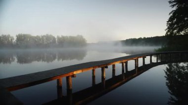 Sabahları göl sisi videosu. Suyun üzerindeki ahşap iskele gün doğumunda gün ışığıyla aydınlatılır. Almanya 'da Mecklenburg Seenplatte' nin sakin ve güzel doğası.