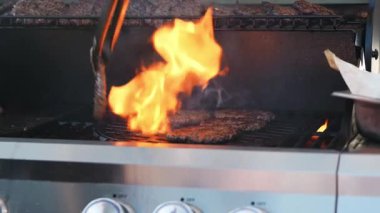 Barbekü ızgarasında köfte çeviriyorum. Sıcak yağ alevlere neden oluyor. Biftek çelik ızgarada yatıyor. Dışarıdaki bir parti için yemek hazırlıyorum..