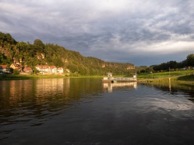 RAthen, Almanya - 16 yaşında. Temmuz 2024: Yaz mevsiminde gün batımında Kurort Rathen 'a tekne karaya çıktı. Elbe Nehri 'nin sakin suları, binaları ve ulusal parkın doğasını yansıtıyor..