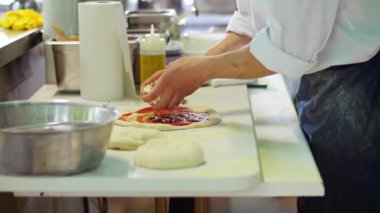 Pizza şefi çiğ hamurun üzerine domates soslu mozzarella peyniri koyuyor. Bir restoranda İtalyan yemeği yapmak. Tepsiyi fırına hazırlıyorum..