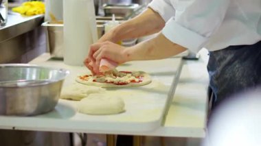 Pizza şefi, peynirli ve domates soslu pizzanın üstüne jambon koyuyor. Bir restoranda İtalyan yemeği yapmak. Sıcak fırın için çiğ yemek hazırlıyorum..