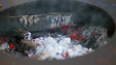 Izgarada parlayan közler. Sıcak kömür çevrede ısı üretiyor. Beyaz kül ve duman delikten çıkıyor. Odundan kömür..