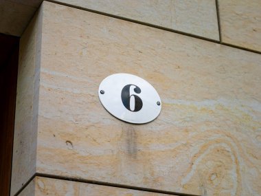 Dış duvarda 6 numara var. Metal plaka emayelidir ve beyaz renklidir. Tasarımı çok eski ve eski. Altı numara bir ev adresinin parçası..