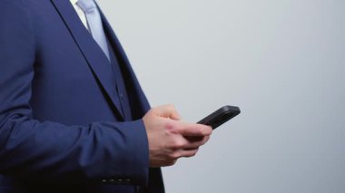 Gri arka planda izole edilmiş cep telefonunu dinleyen bir iş adamı. Meşgul kişi akıllı telefondan araklıyor ya da kaydırıyor.