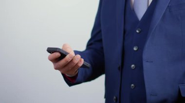 Gri arka planda izole edilmiş cep telefonunu dinleyen bir iş adamı. Genç başarılı kişi mesajlar yazıyor ya da akıllı telefondan kayıyor.