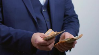 Takım elbiseli bir iş adamı para sayıyor ve elinde 50 Euro 'luk banknotlar tutuyor. Bir insanın çok parası vardır ve zengindir..