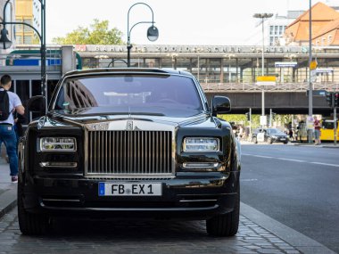 BERLİN, ALMANY - 27. Mayıs 2023, Rolls Royce Phantom lüks arabayı caddenin yanına park etti. Siyah, parlak limuzin boş. Arka planda toplu taşıma binaları var.
