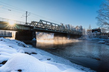 Ilık güneş ışığı donmuş kayaları ve nehir üzerindeki köprüyü aydınlatıyor.