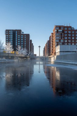 Finlandiya 'nın Tampere kentindeki modern mimari ile çevrili bir kanalın dengeli ve temiz kış manzarası açık gün ışığı altında.