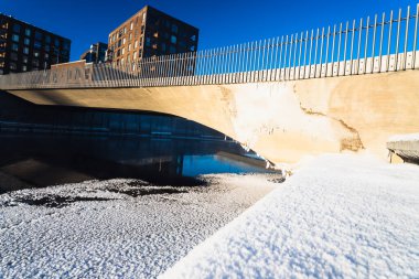 Parlak güneş ışığı, liman boyunca temiz mimari çizgiler ve donmuş dokuların altını çiziyor.