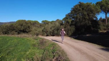 Bir kadın soğuk bir günde zeytin ağaçlarıyla çevrili kırsal bir toprak yolda koşuyor..