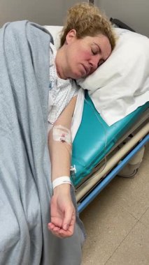 Kadın, hastanede yatıyor, elinde IV 'le tedavi görüyor.