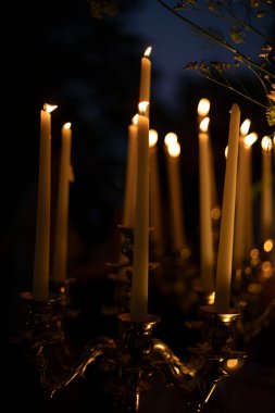 Zarif bir şamdanın üzerinde mum yakar karanlıkta parlar, ılık ve samimi bir atmosfer yaratır, yumuşak altın ışıkla karanlık, bulanık bir arka plana karşı..