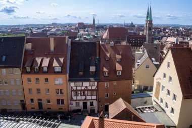 Nürnberg 'in Kaiserburg Nrnberg' deki panoramik manzarasında, açık bir yaz gökyüzü altında Bavyera kereste çerçeveli evler, ortaçağ kuleleri ve kırmızı çatılar yer alıyor..