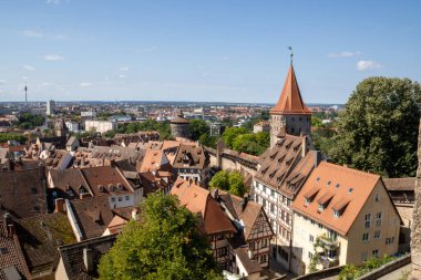 Nürnberg 'in Kaiserburg Nuremberg' deki eski kasabasının panoramik manzarasında, açık bir yaz gökyüzü altında Bavyera kereste çerçeveli evler, ortaçağ kuleleri ve kırmızı çatılar yer alıyor..