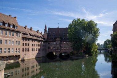 Almanya 'nın Nuremberg kentindeki Heilig-Geist-Spital' de Pegnitz Nehri üzerindeki Museumsbrcke Köprüsü 'nden bakıldığında, tarihi ortaçağ binasının suya yansıyan kemerleri görülüyor..