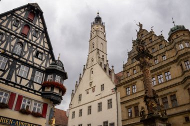 Rothenburg ob der Tauber, Almanya Pazar Meydanı, tarihi belediye binası kulesi, Ratstrinkstube Saat Kulesi, yarım kereste evler, kaldırım taşı sokaklar, Bavyera kentinde çeşme ve dükkanlar.