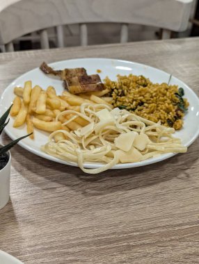 İçinde kremalı fettuccine makarna, parmesan talaşı, altın patates kızartması, yeşillikli baharatlı pirinç ve kızarmış domuz dilimleri olan çeşitli bir yemek. Güçlü bir karbonhidrat ve protein karışımı..