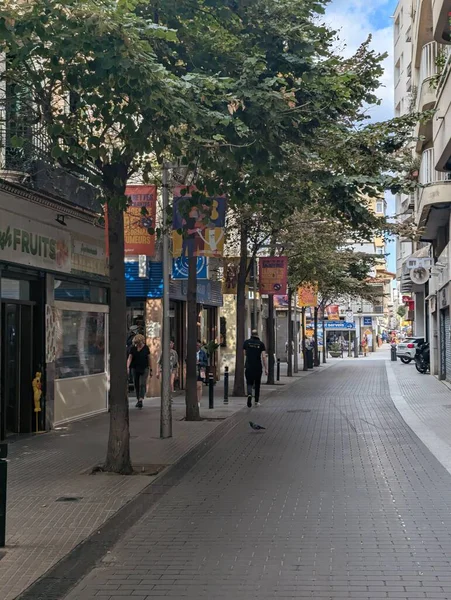 Lloret de Mar İspanya 13 Eylül 2024 Dar Yaya Caddesi Dükkanlarla, Ağaçlarla ve Mağazalarla çevrili, Sessiz Öğlen Atmosferi, Yolcu Çantasıyla Geziniyor, Hafıza Çantasıyla Yumuşak Gölgeler, Bollards