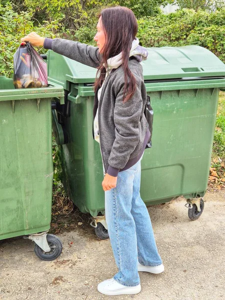 Bir kadın çöp torbasını çöp kutusuna atıyor. Açık hava atık imhası. Fotoğraf bir ev atığı imhası ve çevresel koruma durumunu gösteriyor.. 