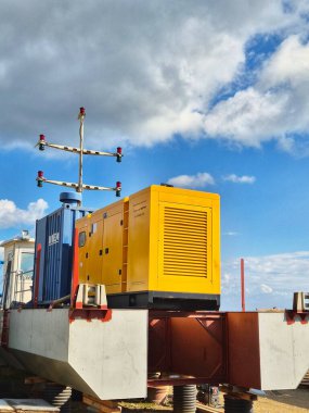 Yüksek bir açık hava platformunda büyük sarı bir dizel güç jeneratörünün (veya endüstriyel elektrik santralinin) fotoğrafı. Endüstriyel dizel güç jeneratörü. Lojistik merkezindeki sarı güç ünitesi. Dramatik bir gökyüzüne karşı yedek jeneratör