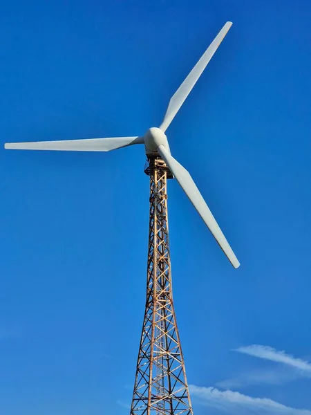 Rüzgar türbininin dikey görüntüsü. Uzun, açık bir kafes kulesi üç bıçaklı pervaneyi destekler. Zengin, bulutsuz (veya neredeyse bulutsuz) kobalt mavi gökyüzü maksimum kontrast ve görsel berraklık sağlar.